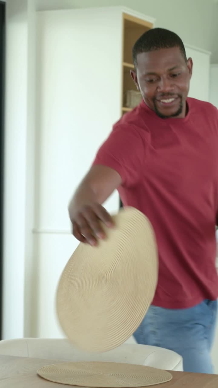 Vertical video: Entering with mats and glasses, man in maroon shirt arranging table, preparing meal