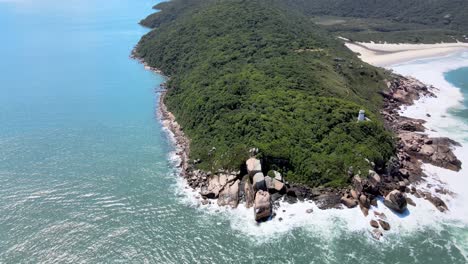 aerial drone scene approaching a rocky and mountainous coastline. zoom in, filled with atlantic forest vegetation with mountain ranges near the beach, blue sky and turquoise sea. naufragados beach