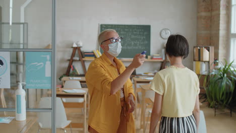 Profesor-Enmascarado-Comprobando-La-Temperatura-De-Los-Estudiantes-Antes-De-La-Lección