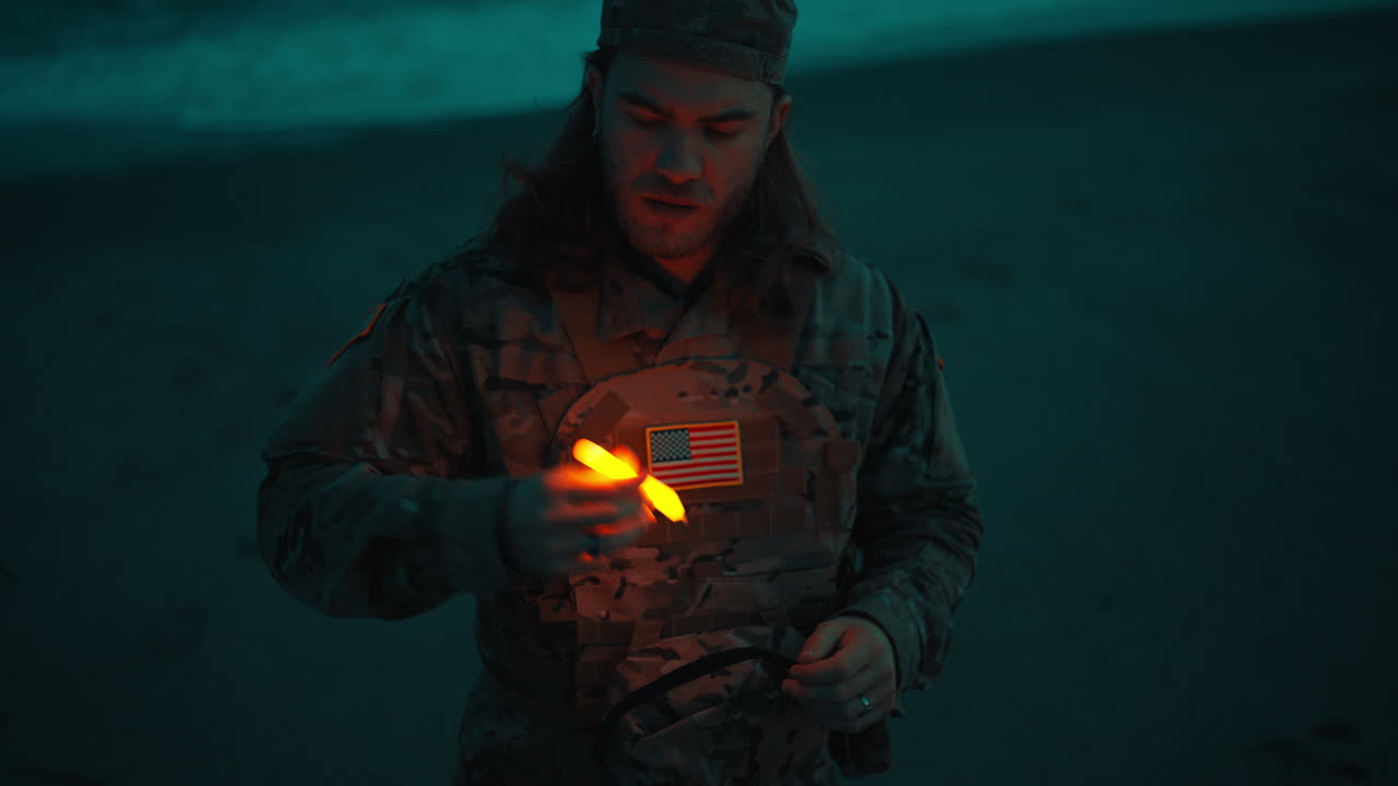 Amerikansk militærmand tænder kemisk lys på stranden nær havet om natten