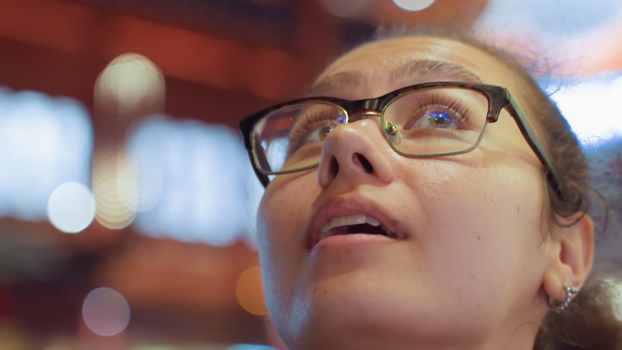 Un'adolescente guarda gli schermi colorati di una sala giochi. La giovane donna esamina con curiosità e fascino i display luminosi al neon, investigando con meraviglia e attenzione concentrata.