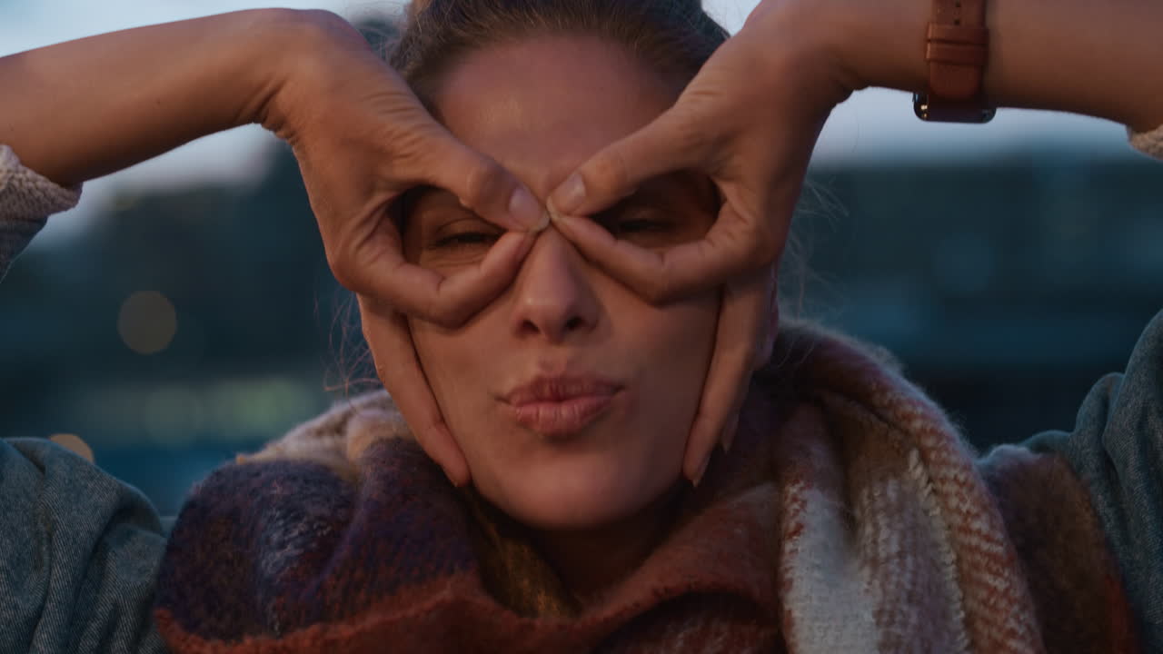 아름다운 젊은 백인 여성이 포즈를 취하고 재미있는 얼굴을 하고 해가 지는 날 지붕에서 축제를 즐기고 키스를 불어넣고 도시에서 즐거운 주말을 보내고 있습니다.