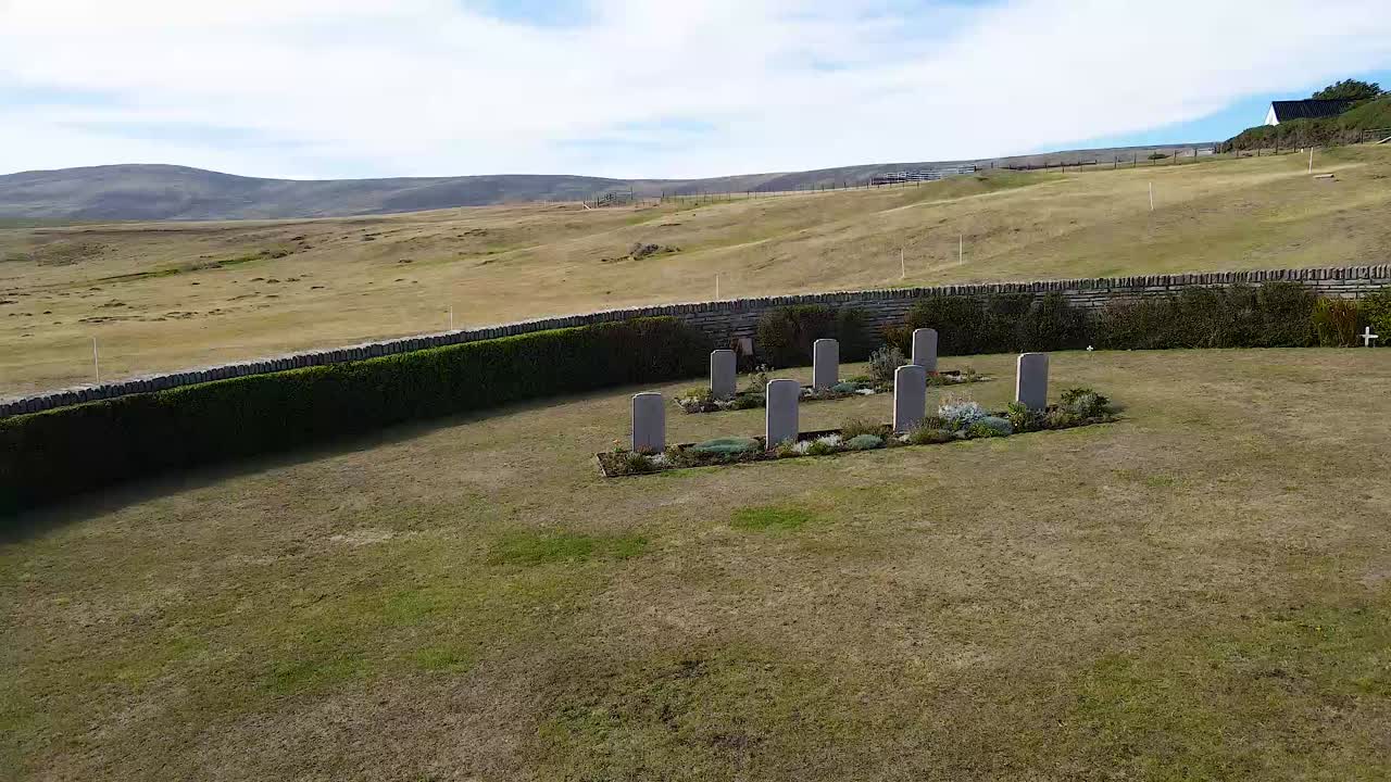 Ruch kamery uchwyca odległe miejsce pochówku na Falklandach, podkreślając jego ponurą atmosferę i znaczenie historyczne.