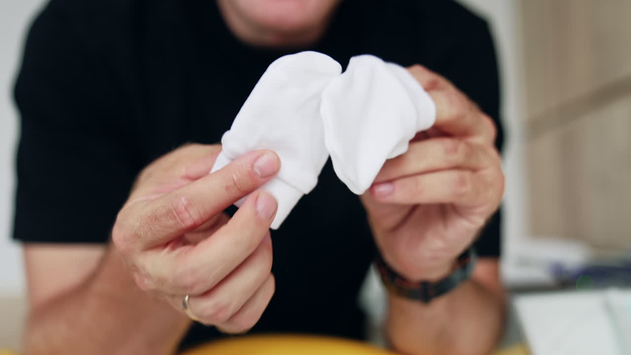 Hands of unrecognized Caucasian male holding tiny white baby socks. Expecting dad showing child's clothes. Close up.
