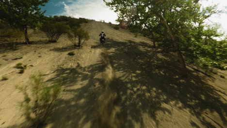 motorcyclist rides uphill in dust cloud fpv drone. professional racer in uniform competes for leadership in extreme racing. motocross route at highland