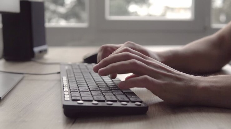 Tippen auf einer Tastatur. Mann tippt auf Computertastatur. Männerhand benutzt Computertastatur und Maus zum Tippen. Freiberuflicher Fotograf arbeitet am Computer.