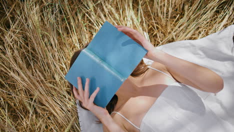 mujer acostada leyendo un libro en un lugar de heno de cerca. bruneta descansando escondiendo la cara