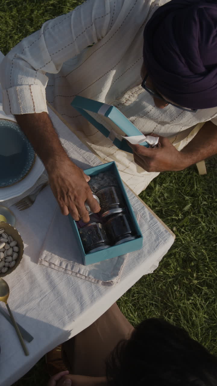 Person Unboxes a Gift with Jars of Food Items at an Outdoor Picnic