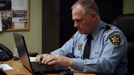 a dedicated officer engaged in computer work at his desk, focusing on important tasks in a law enforcement setting with attention to detail and professionalism