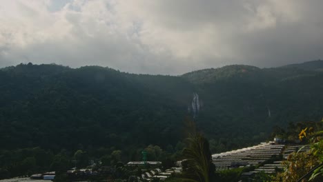 mountain landscape with waterfall and greenhouses under cloudy sky