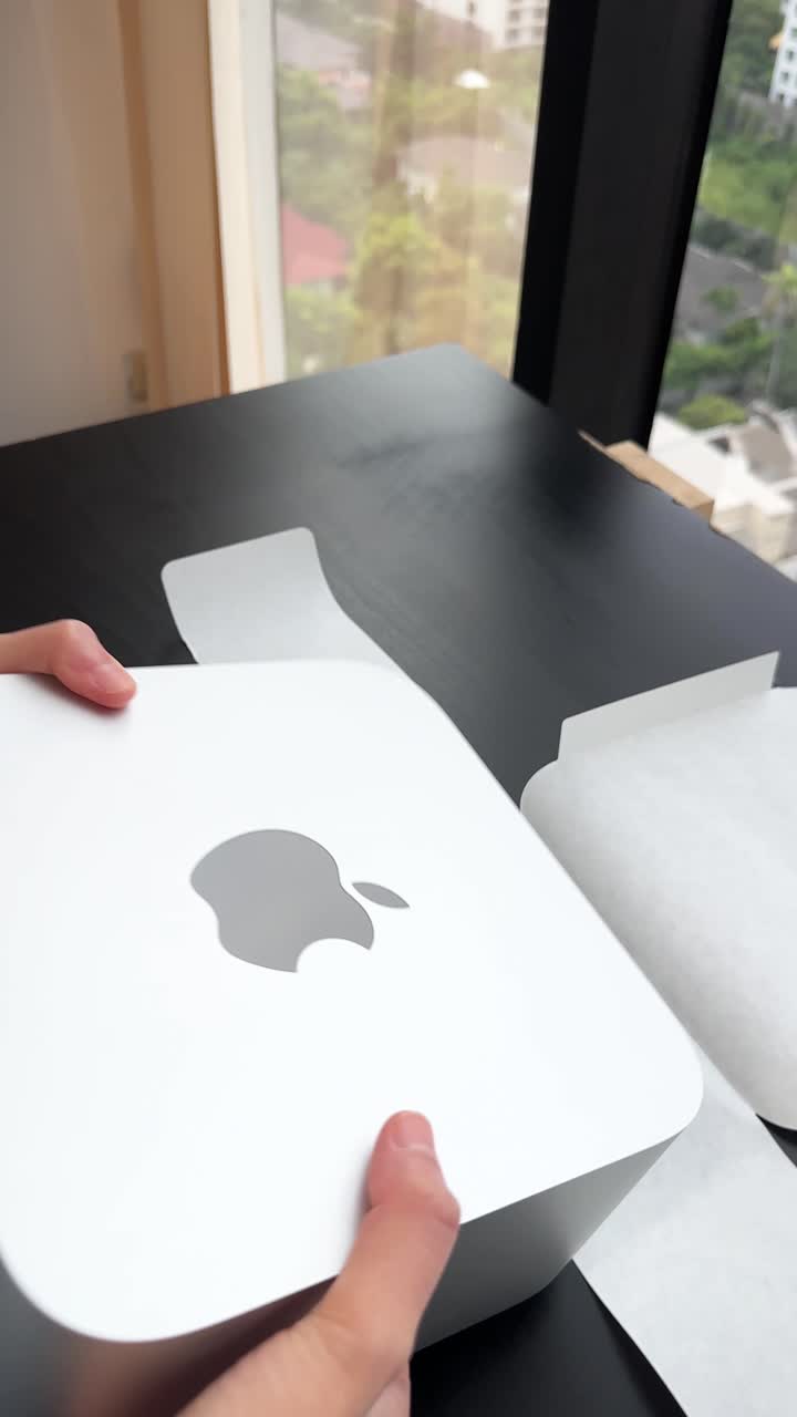 Hands unbox compact desktop computer on black table, natural daylight, high-rise city view background