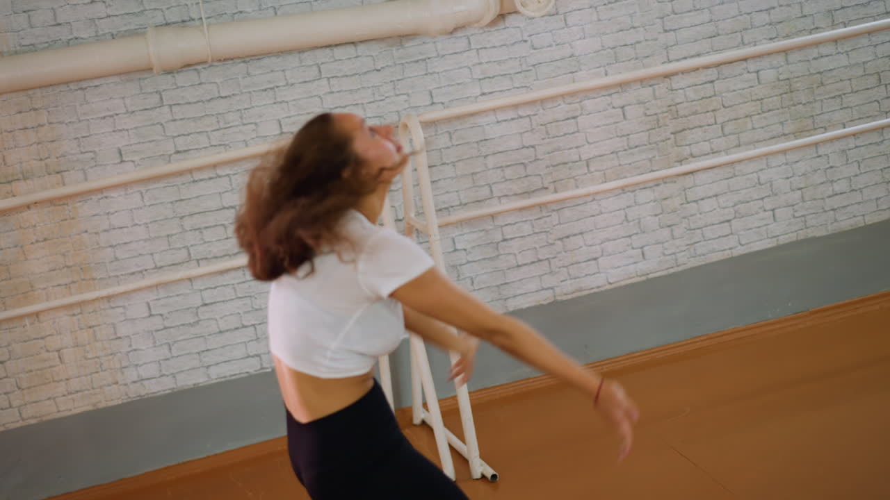 Lady in white top and black leggings dancing with full energy inside studio flipping hair and moving with intensity showing expressive style strength and powerful rhythm