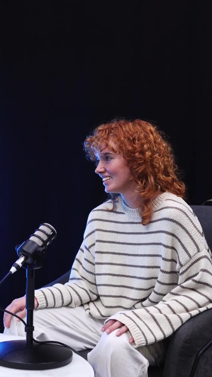 Giovane donna sorridente con capelli rossi ricci che registra un podcast
