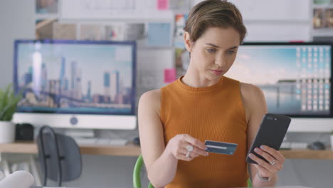 female architect in office working at desk making online purchase using credit card on mobile phone