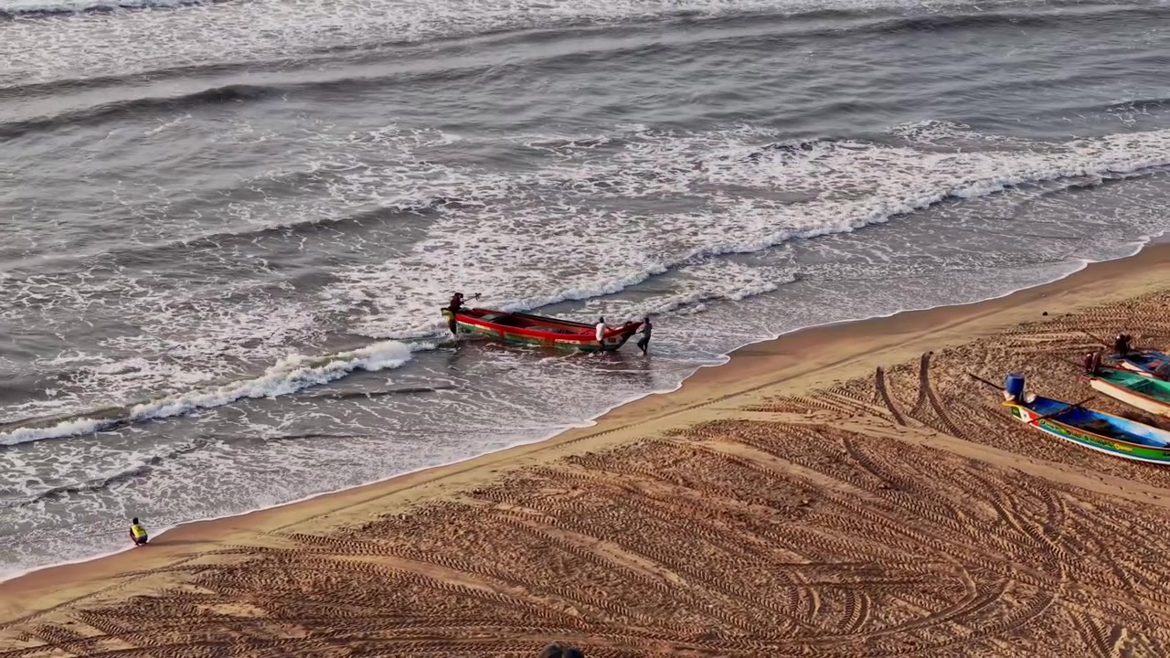 Ripresa aerea con drone di un peschereccio che si avvicina alla spiaggia di Chennai attraverso le onde del Golfo del Bengala mentre i pescatori si preparano ad approdare sulla riva sabbiosa nel Tamil Nadu, India.