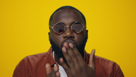 retrato de un apuesto hombre afro enviando un beso en el aire a la cámara sobre un fondo amarillo.