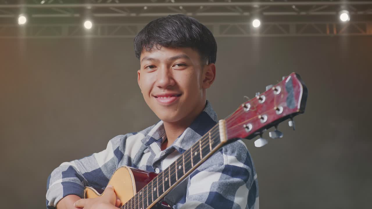 기타를 들고 무대에서 팔을 고 미소 짓는 아시아 십대