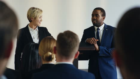 caucasian woman and african american man on a podium in front of the auditory and presenting a project at a conference