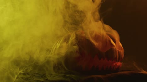 video of halloween carved pumpkin with smoke and orange light on black background