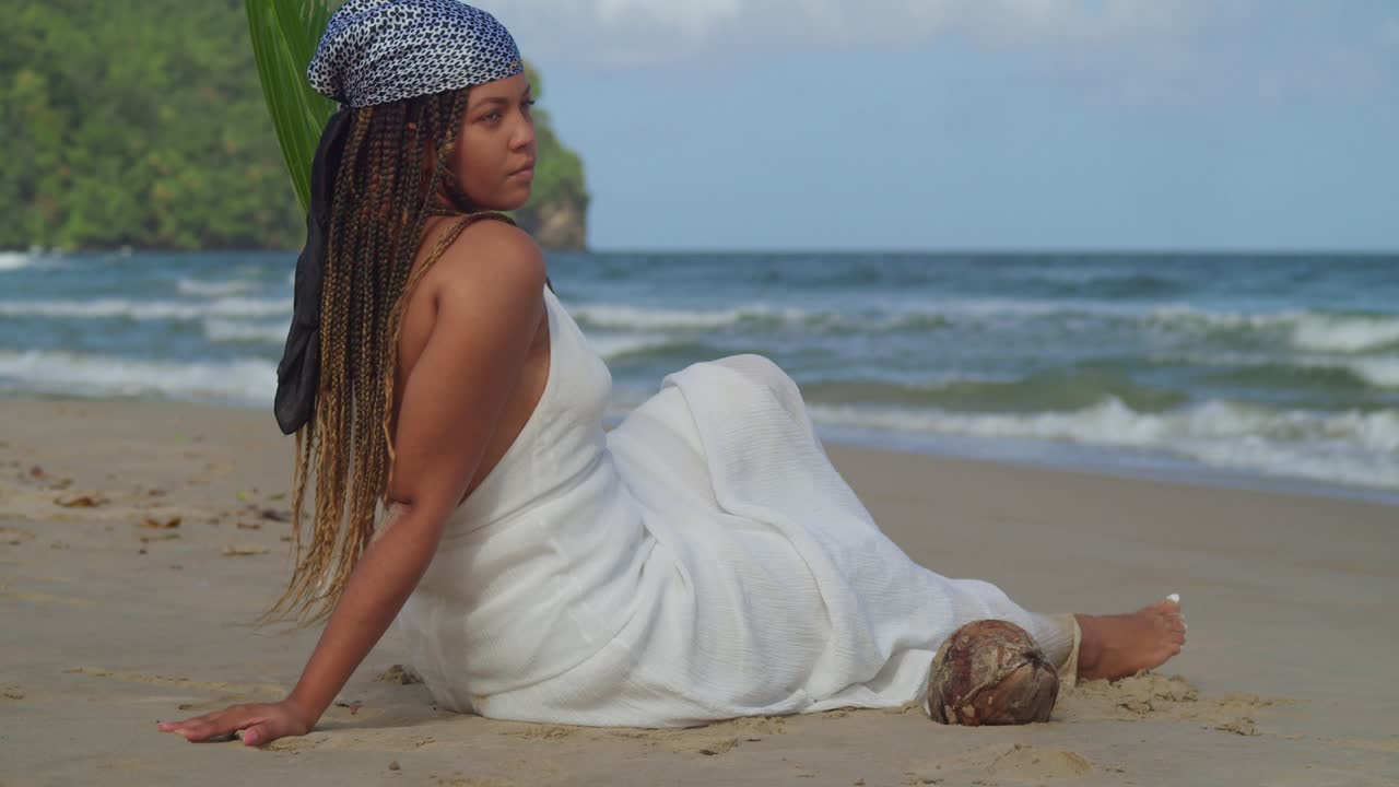 panorámica de la cámara izquierda de una joven sentada en la playa mientras disfruta de la brisa marina