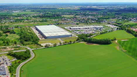 Buildings-of-logistics-center,-warehouses-near-the-highway,-view-from-height,-a-large-number-of-trucks-in-the-parking-lot-near-warehouse