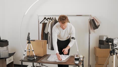 general plan, cute curly young man packs clothes in a cardboard box to send