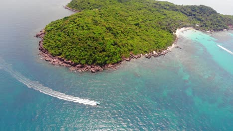 Vista-Orbital-Aérea-De-Lancha-Rápida-Navegando-En-El-Océano-Turquesa-Cerca-De-La-Costa-Rocosa-De-Una-Isla-Tropical-Verde-Salvaje-En-El-Archipiélago-De-Vietnam,-Paisaje-De-Phu-Quoc