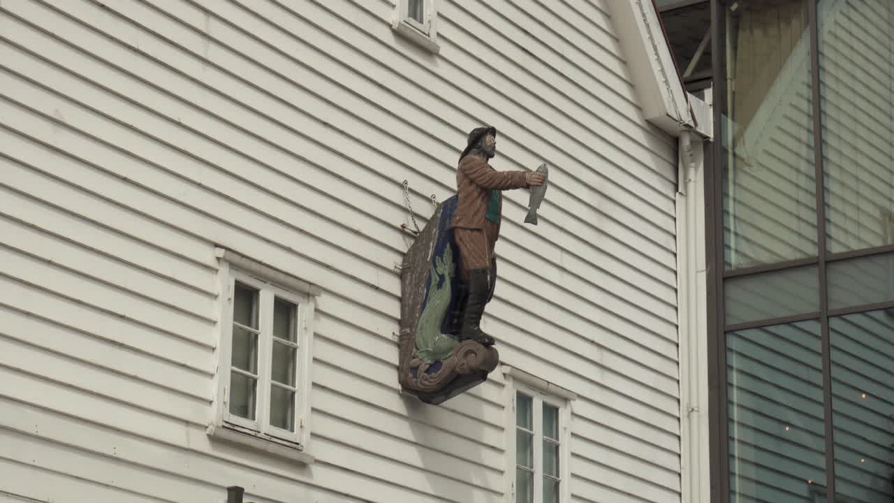 Fisherman Sculpture Holding A Fish, Mounted On The Exterior Of A Bar Near The Fish Market In Bergen, Norway. - wide shot