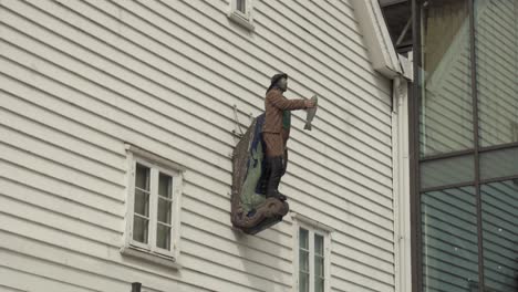 fisherman sculpture holding a fish, mounted on the exterior of a bar near the fish market in bergen, norway. - wide shot