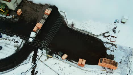 aerial overhead shot of forklift unloading wooden forms from white semi truck in winter and stacking them in the yard