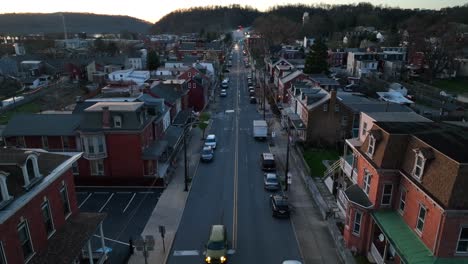 Descending-drone-shot-of-car-driving-on-main-street-in-american-city-during-dusk