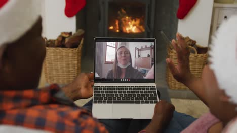 Pareja-Afroamericana-Con-Sombreros-De-Santa-Usando-Una-Computadora-Portátil-Para-Una-Videollamada-Navideña-Con-Una-Mujer-En-La-Pantalla