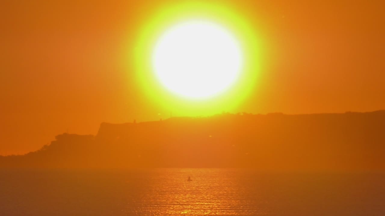 Big glowing sun rising over calm seas, coastal seascape