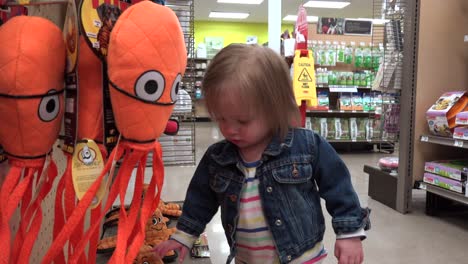 toddler shopping at pet store at orange stuffed animal dog toy section.