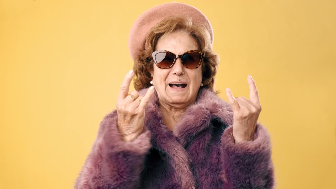elegante mujer mayor haciendo un gesto de rock n roll con sus dedos sobre un fondo amarillo