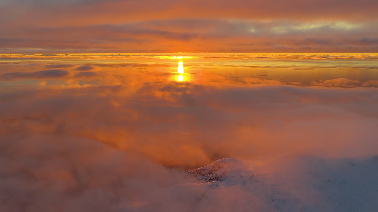 Breathtaking aerial view of a golden hour sunset reflecting on a sea of clouds above the snowcapped peaks of Lofoten, Norway