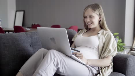 smiling pregnant woman shopping online with laptop