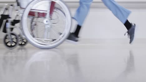 lowsection of african american male doctor running with wheelchair in hospital corridor, slow motion