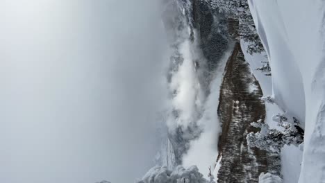 Impresionante-Paisaje-Invernal-Con-Toma-Vertical-Mirando-Hacia-Un-Valle-Nublado-Cubierto-De-Nieve-Desde-La-Cima-De-Una-Estación-De-Esquí-En-Las-Montañas-Rocosas-De-Utah-En-Un-Día-Frío-Y-Nublado