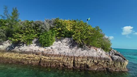 rotating action camera wide shot passing by a rocky tropical cliff and turquoise clear water below from a tourist boat in the bahamas on a warm sunny summer day