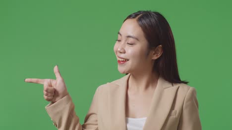 close up of asian business woman with a smile pointing to the side while standing in the green screen