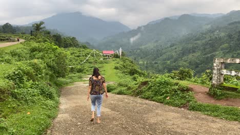 Rear-view-of-Happy-young-Indian-girl-walking-through-mountain-roads-enjoying-her-vacation-or-outing-at-hill-top-in-India