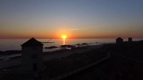 4k-Schwenk-Nach-Rechts-Luftaufnahme-Von-Windmühlen-In-Der-Nähe-Der-Meeresküste,-Die-Einen-Wunderschönen-Sonnenuntergang-Enthüllt