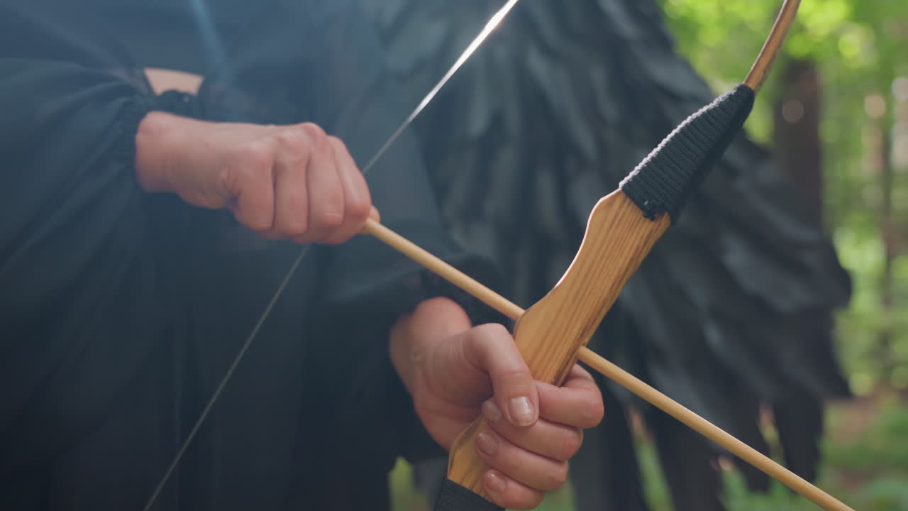 Close up of hands gripping wooden bow and drawing arrow in green forest, sunlight reflecting on polished wood, capturing tension, focus, and calm strength in moment before release