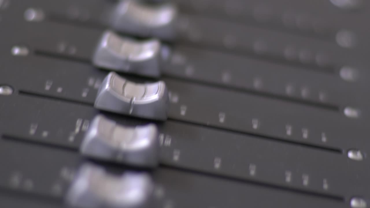 Close up panning shot from above of silver faders on a mixing audio console in a recording studio
