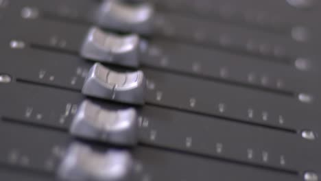 primer plano panorámico desde arriba de los faders plateados en una consola de mezcla de audio en un estudio de grabación