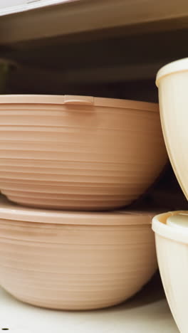 vista de una exhibición cuidadosamente dispuesta de cuencos de varios tamaños y colores en los estantes de las tiendas. los cuencos son de colores verde, marrón y beige