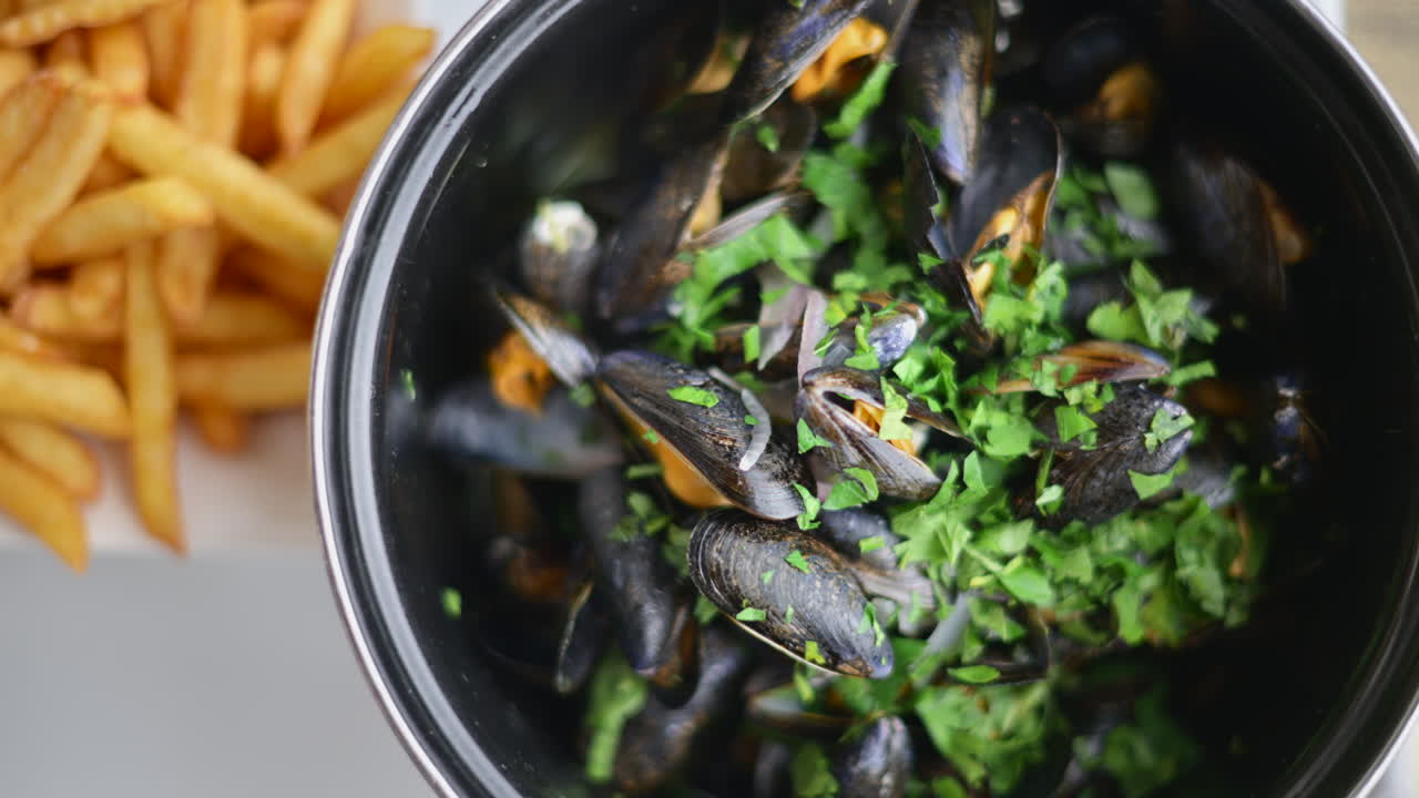 Cooked mussels served in a pot with herbs and sauce, accompanied by golden fries on the side