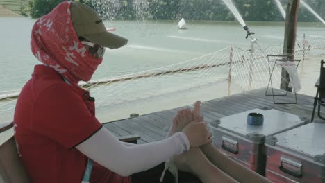 a person wearing a hat and face covering is using ice to treat the burned foot of another individual, seated near a lakeside deck