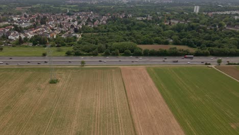 Static-aerial-time-lapse-of-numerous-cars-driving-along-a-freeway-between-fields-and-a-village-in-Hesse,-Germany